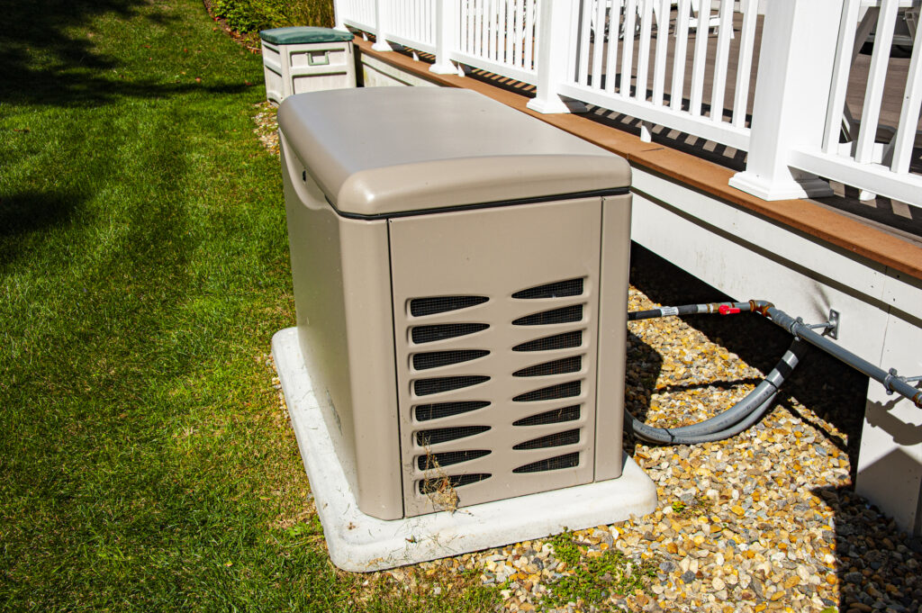 Residential standby generator on concrete pad next to the raised deck of a home.